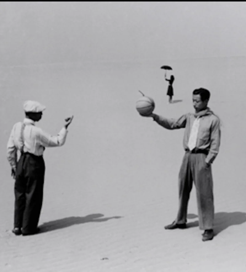 Two men in the desert, woman in the background with an umbrella