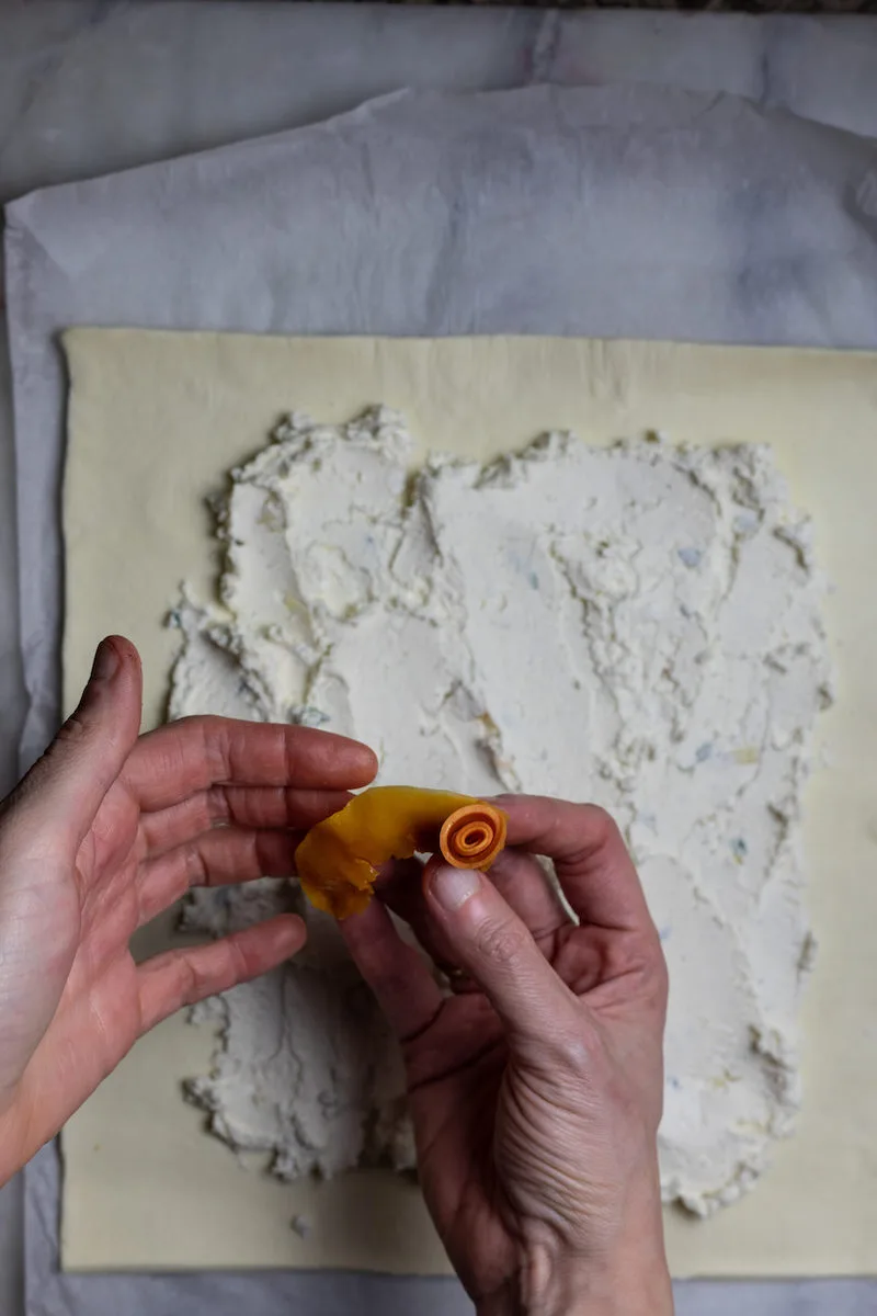 Photography of someone creating a rose out of food with puff pastry and flours in the background